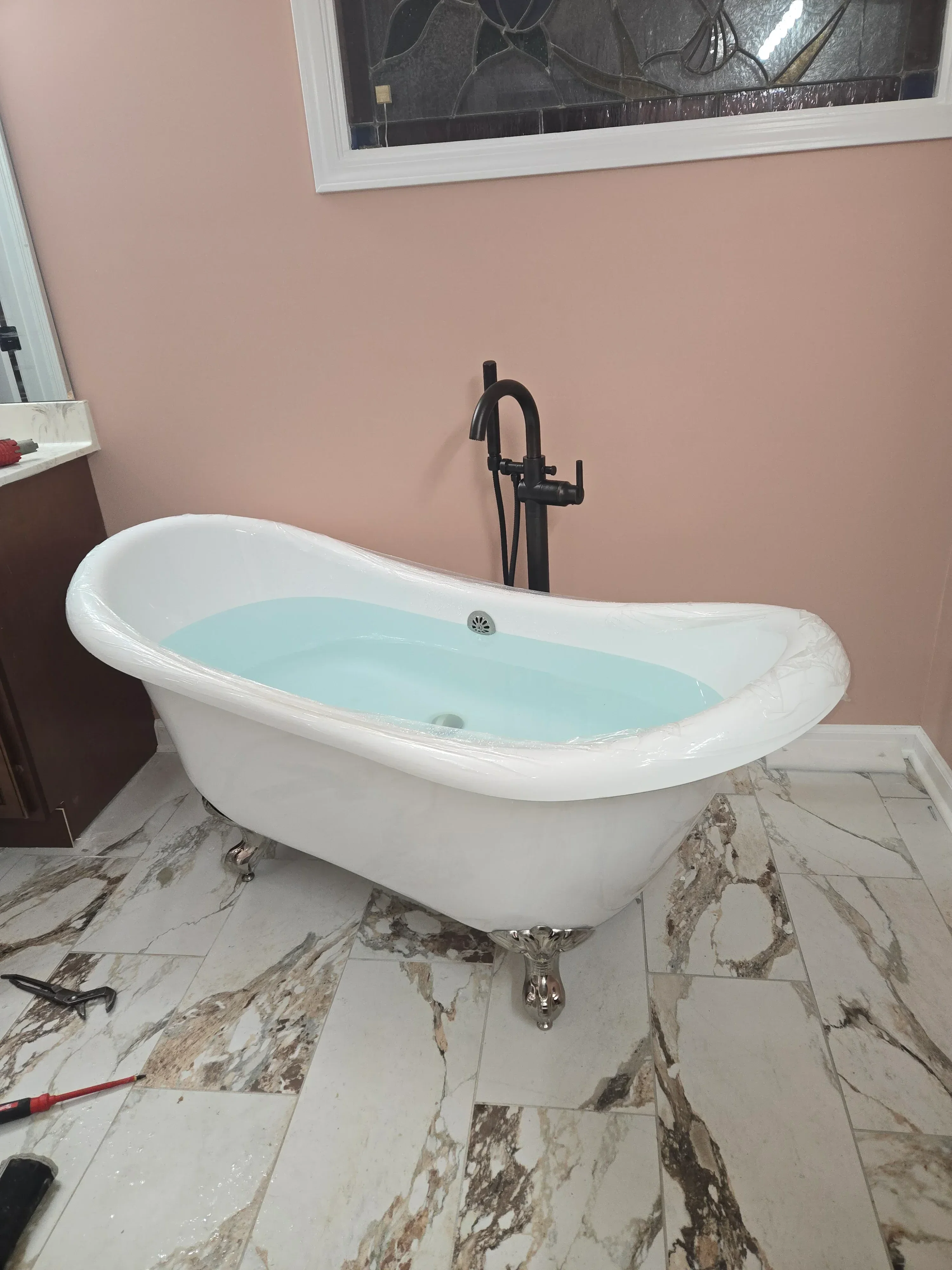 White soaking tub with turquoise interior and chrome fixtures installed against marble tile wall