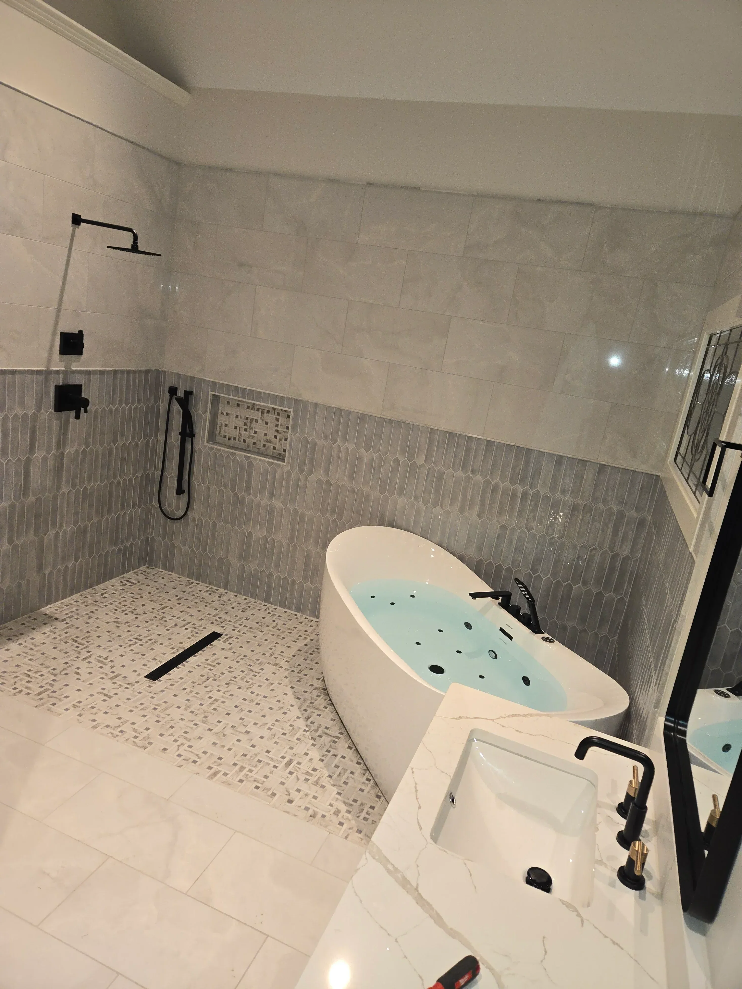 Freestanding soaking tub with white and light blue finish, black fixtures, subway and linear tile installation
