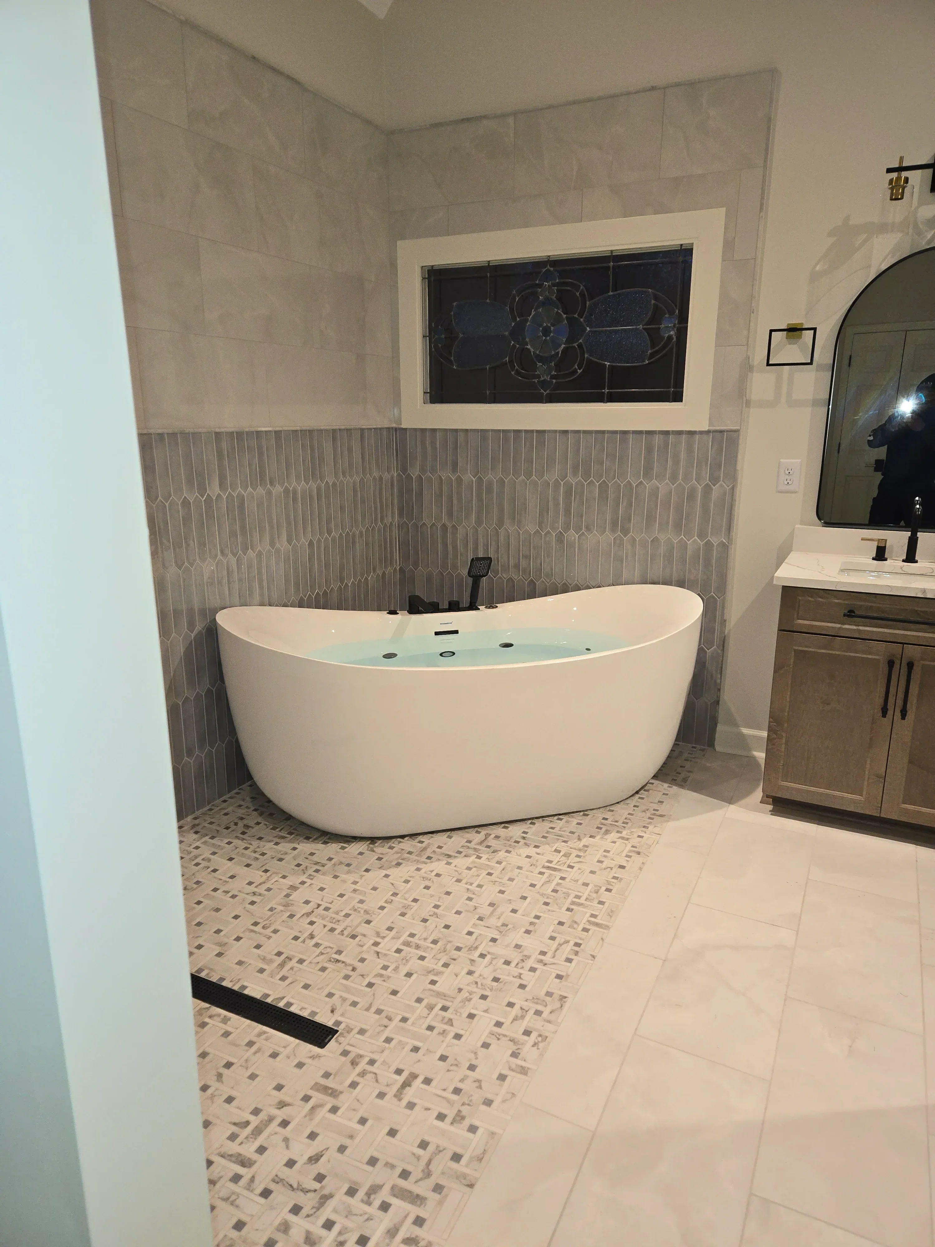 Bathroom with gray linear floor tile, white subway walls, mosaic accent tile, and white exhaust fan installation