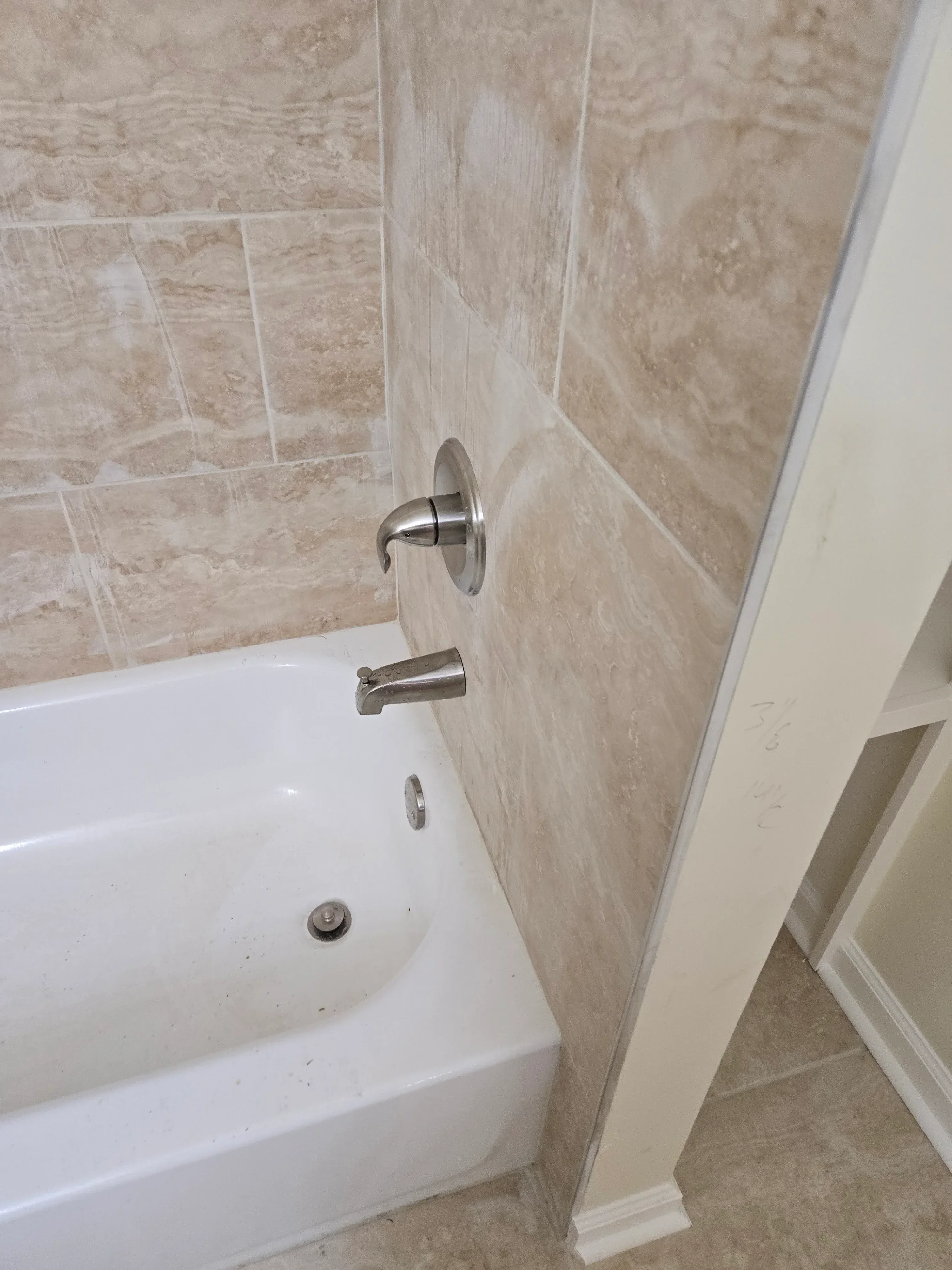 Chrome wall-mounted faucet and towel bar above white sink with travertine tile surround