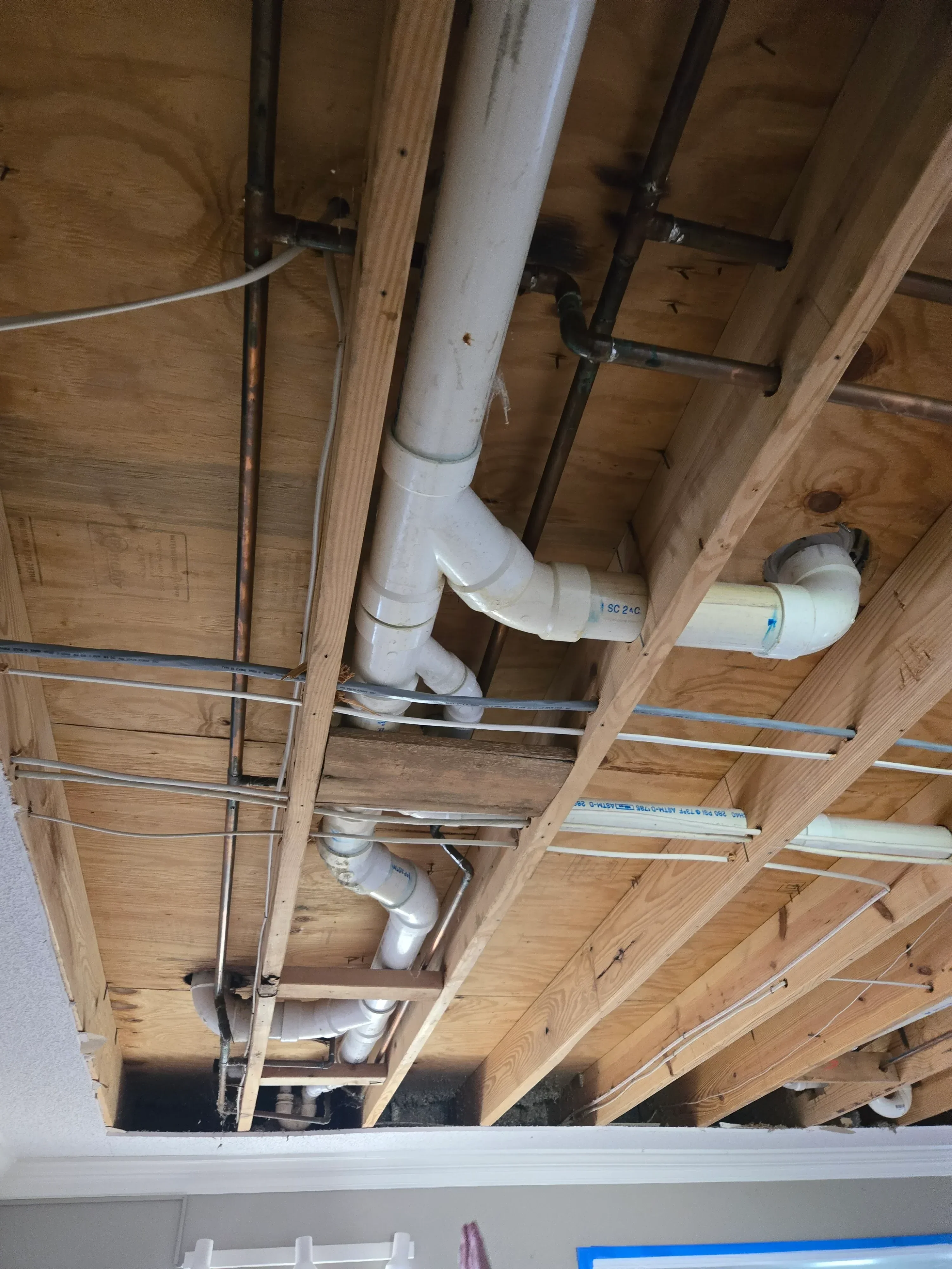 White PVC ductwork with elbows and fittings installed in wooden framed ceiling cavity with metal strapping