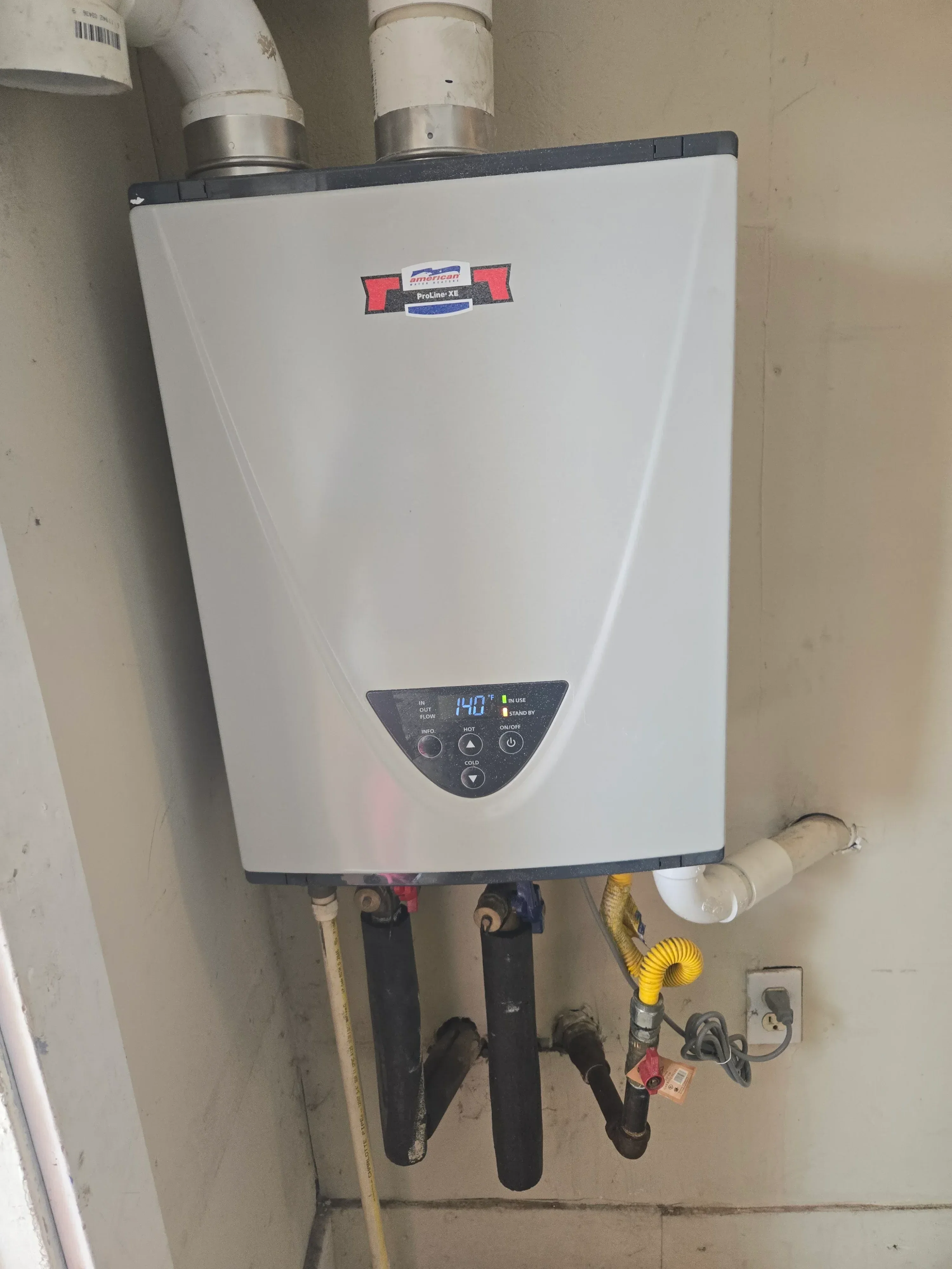 Tankless water heater with digital controls, venting ducts, and isolation valves installed on concrete wall