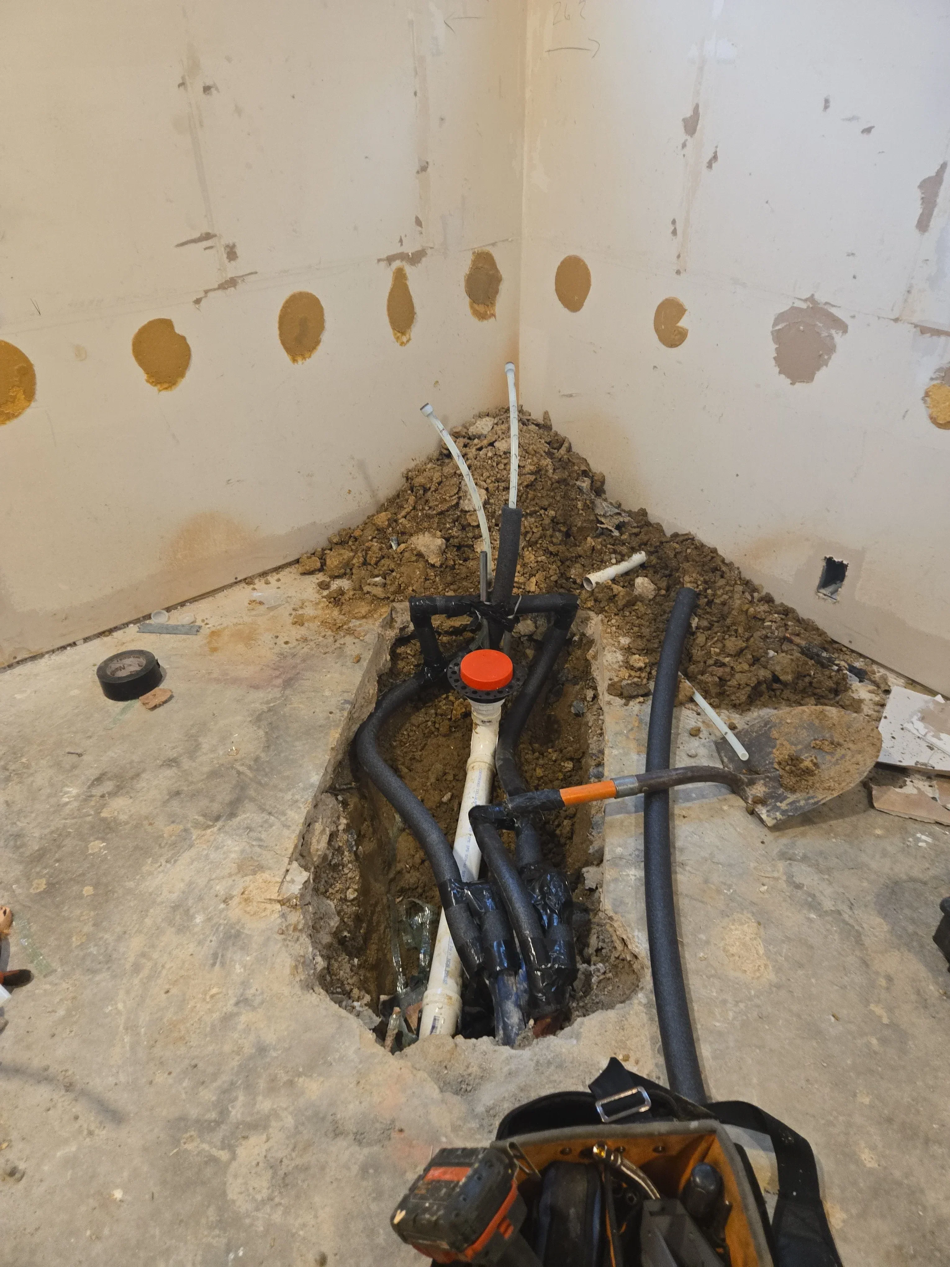 Black electrical conduit installation in concrete foundation with soil excavation and protective wrapping