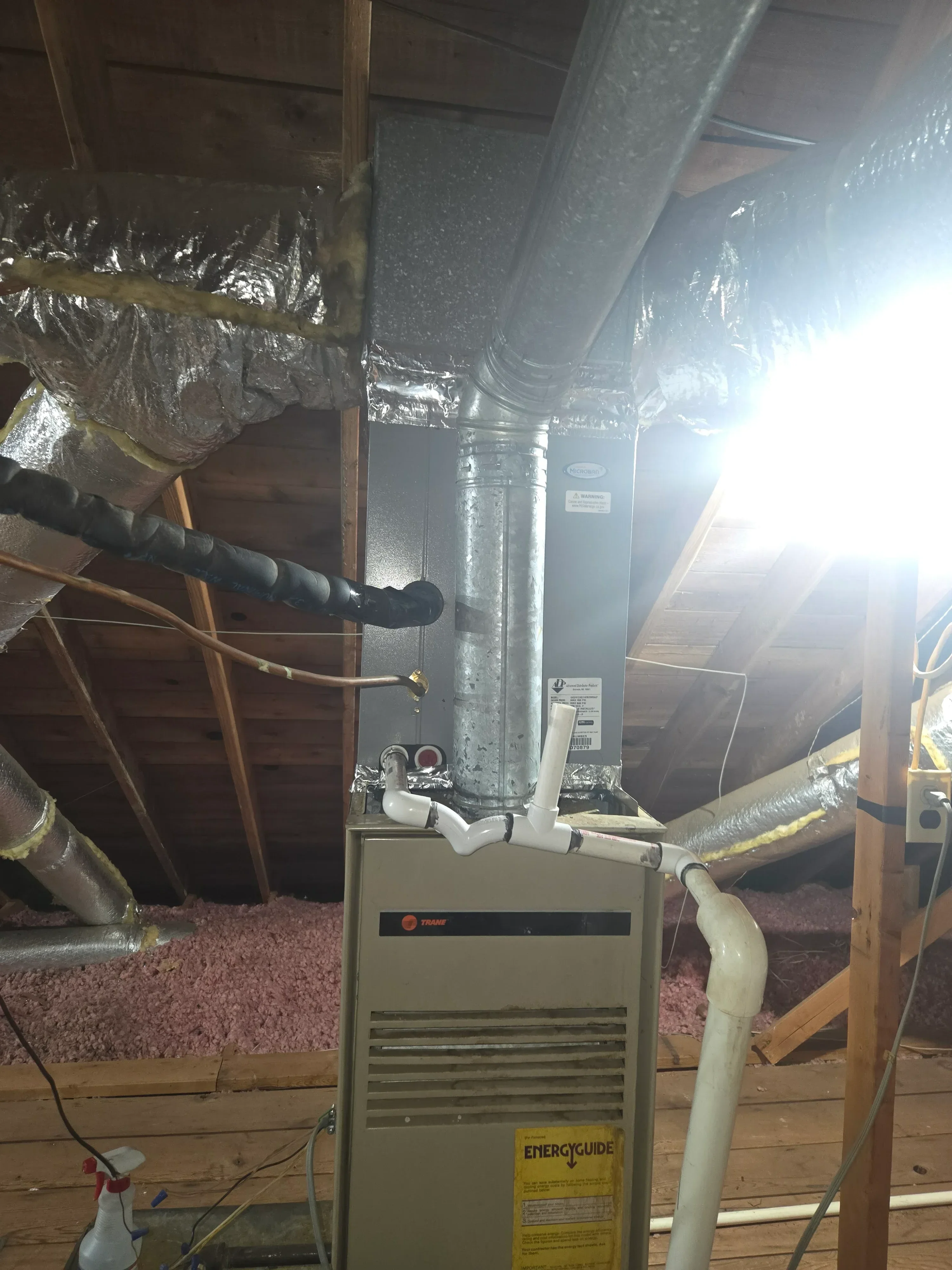 Furnace unit with insulated metal ductwork, white PVC piping, and control panel in attic installation