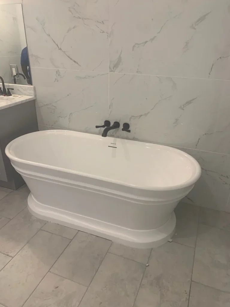 Freestanding white soaking tub with marble-look tile walls and flooring in modern bathroom