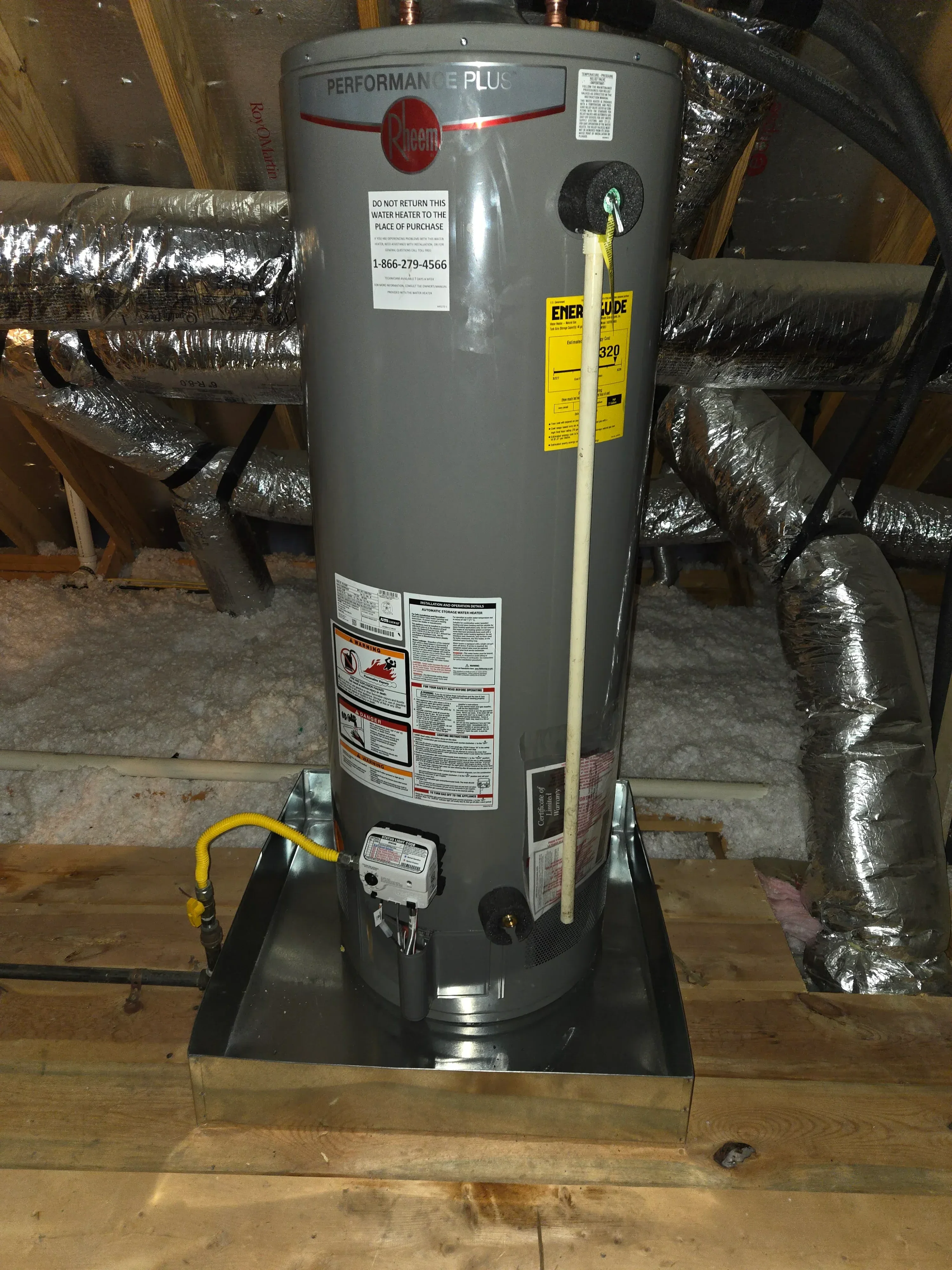 Gray electric water heater with insulated copper piping and yellow safety labels installed in utility space