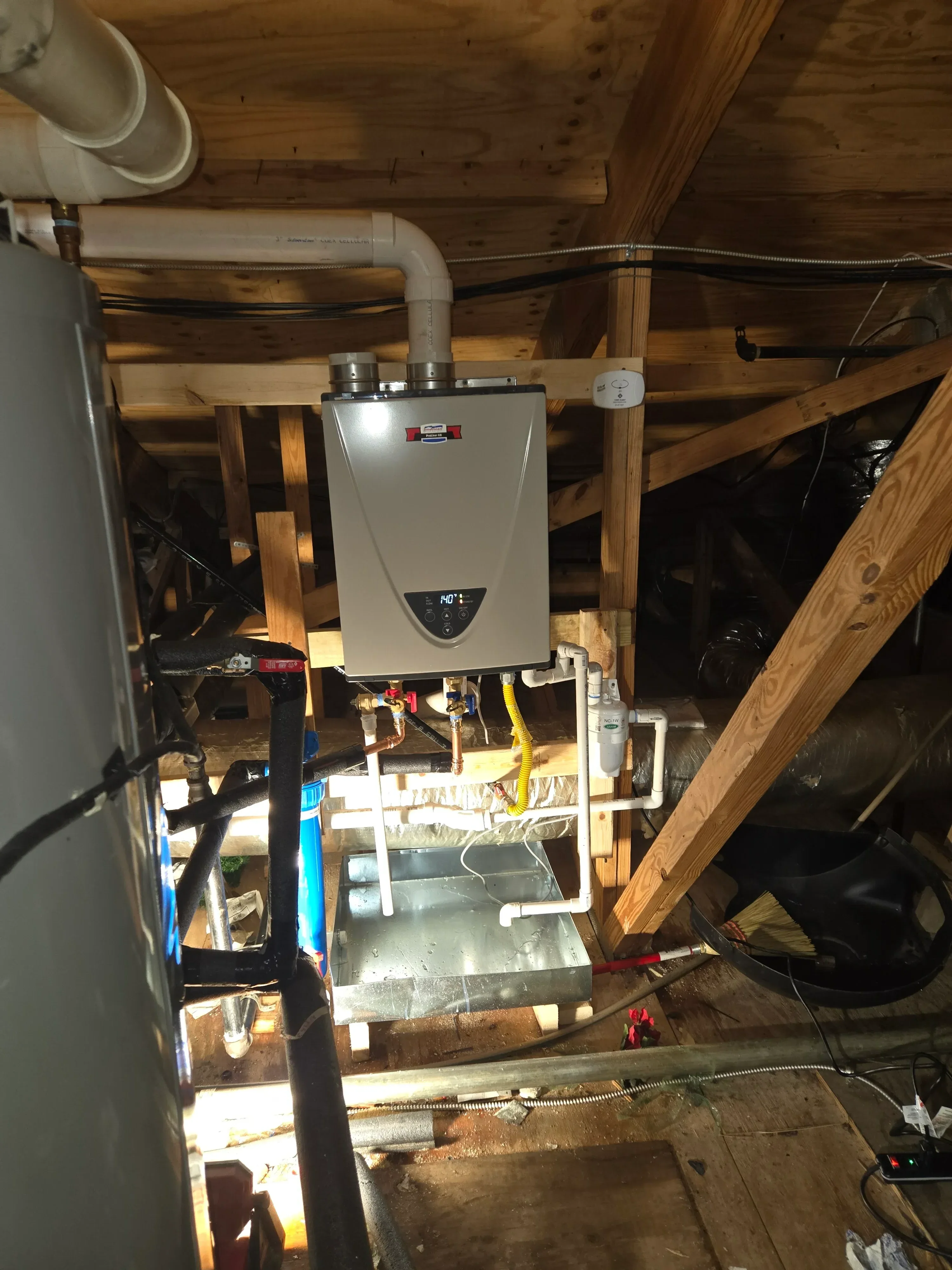 Tankless water heater mounted on PVC brackets in attic with copper piping and white exhaust vent