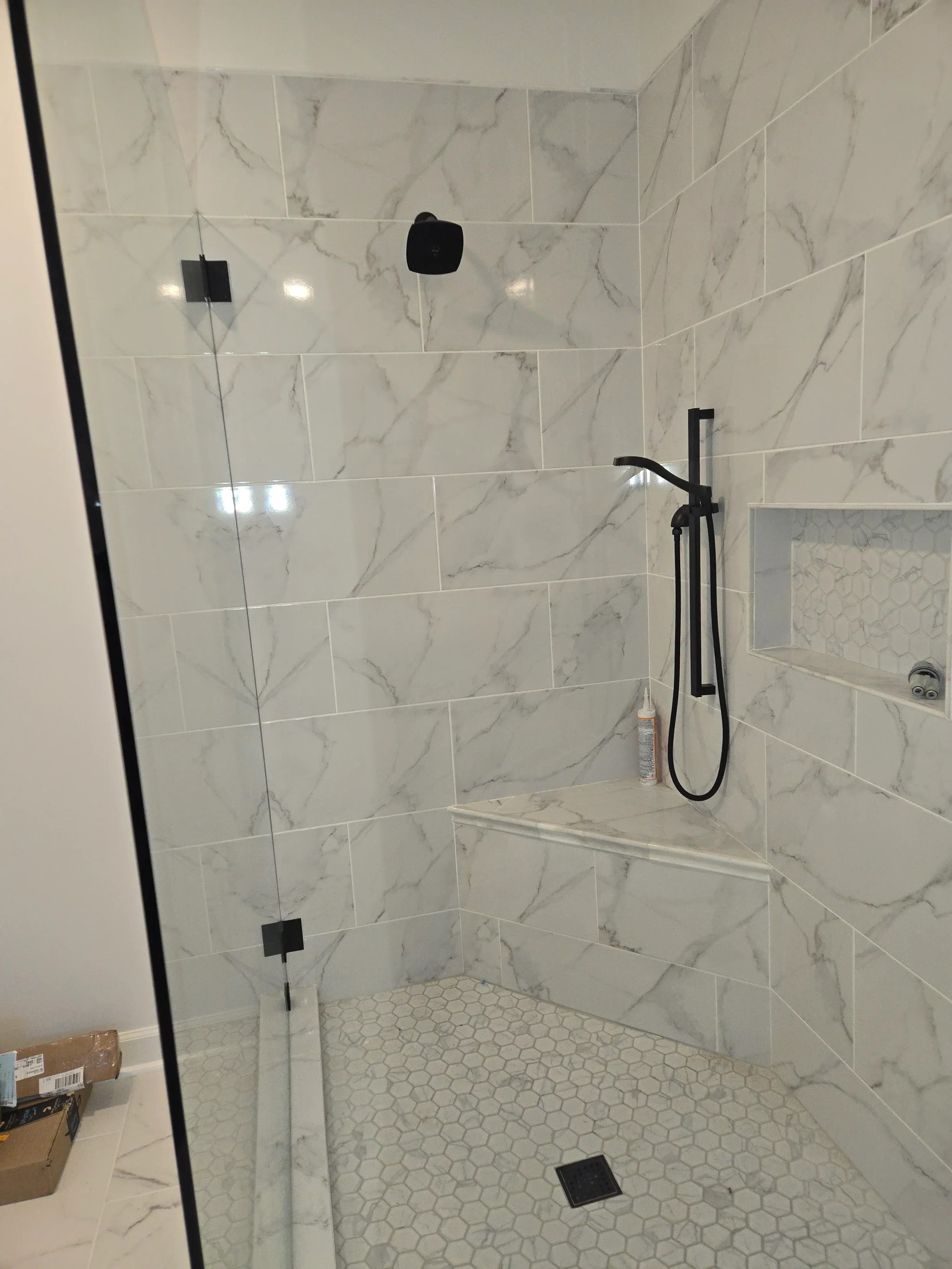 Marble tile shower with black fixtures, hexagonal accent wall, and recessed ceiling detail
