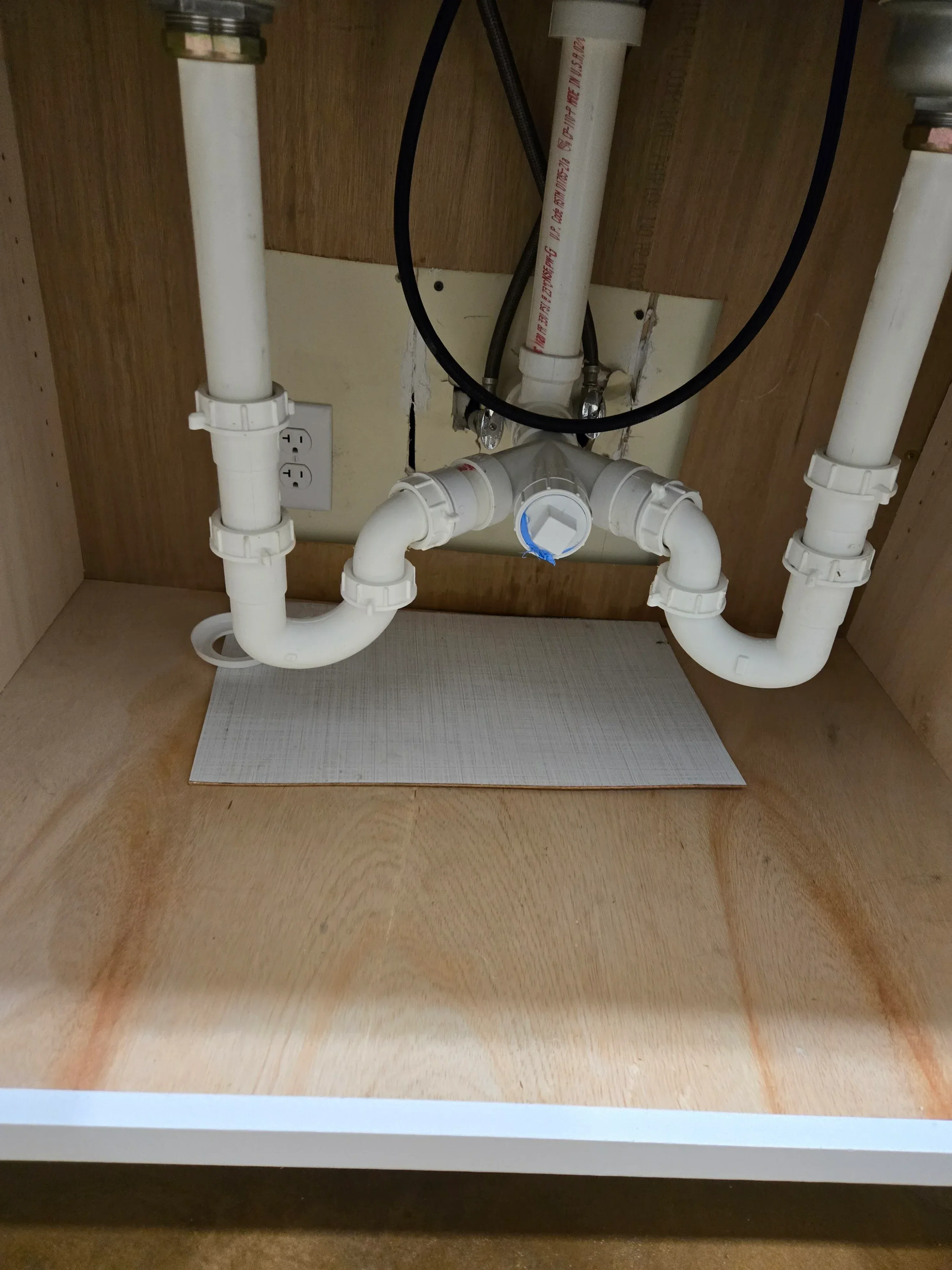 White PVC pipes, shut-off valves, and drain lines installed under kitchen sink cabinet